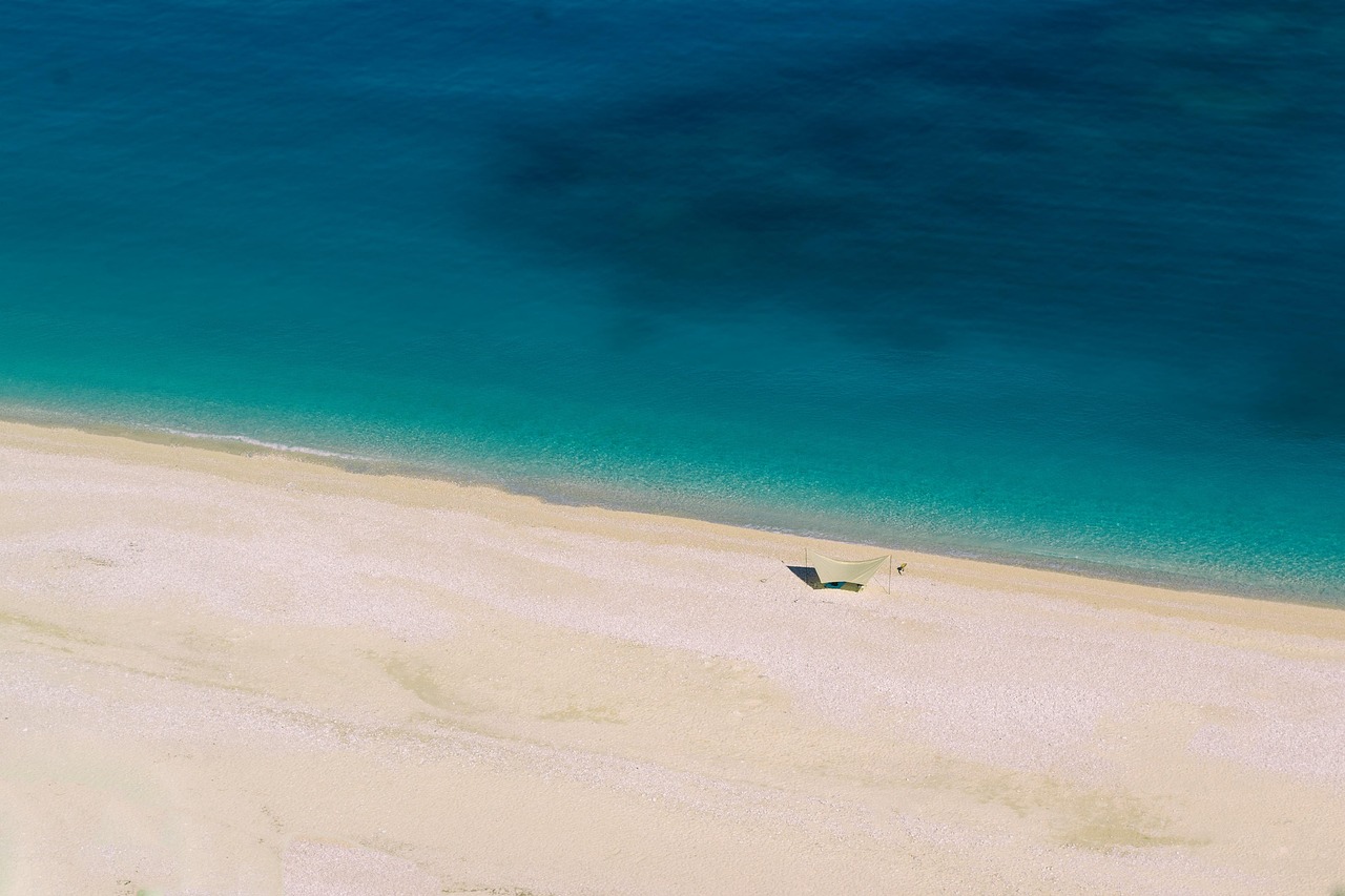 Spiaggia con acque che mutano tonalità, mostrando sfumature blu e verdi sotto il sole.