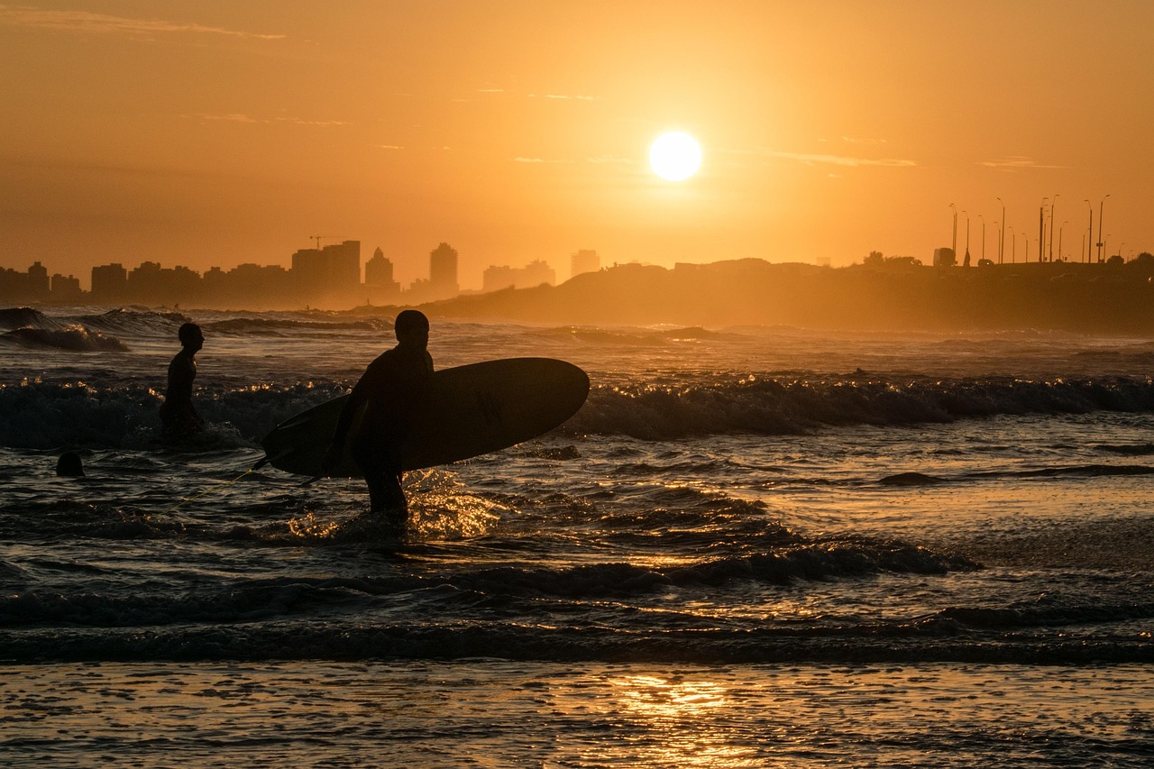 Spiaggia affollata di surfisti che cavalcano le onde al tramonto.