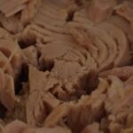 Immagine di diverse lattine di tonno in scatola con etichette di marchi famosi e avvertenze sulla salute.