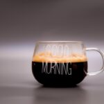 Un caffè fumante con una tazza su sfondo luminoso, simbolo di un buongiorno virtuale tra amici.