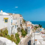 Borgo siciliano con case bianche e blu, arroccato su scogliere a picco sul mare.