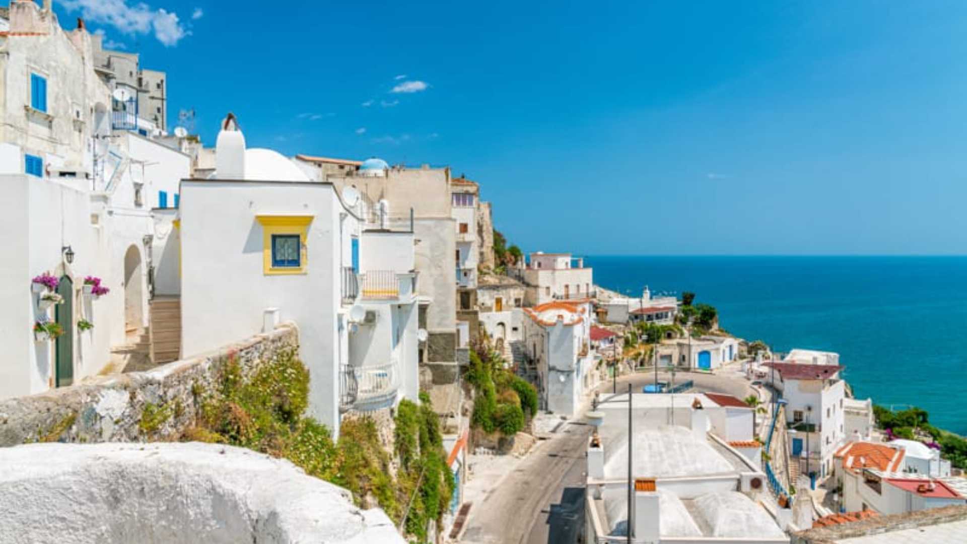 Borgo siciliano con case bianche e blu, arroccato su scogliere a picco sul mare.