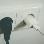 Interruttore e presa elettrica sporchi, con batteri visibili e prodotti per la pulizia accanto.